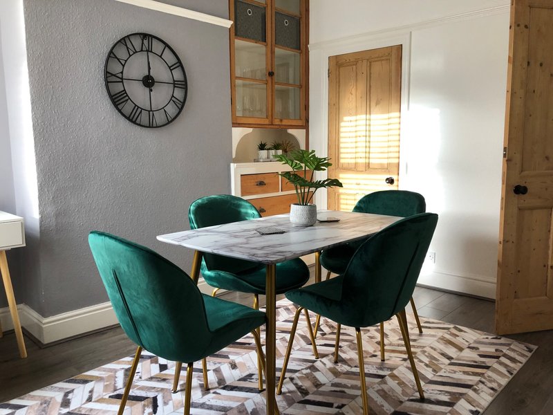 Dining room with marble table, teal and black chairs, wall clock, and geometric rug