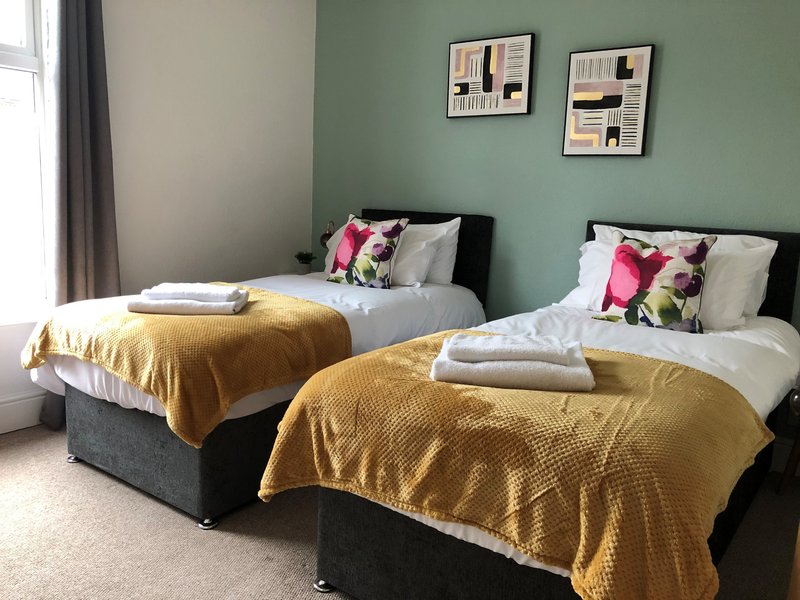Twin bedroom with yellow bedspreads, colorful cushions, green accent wall and framed artwork