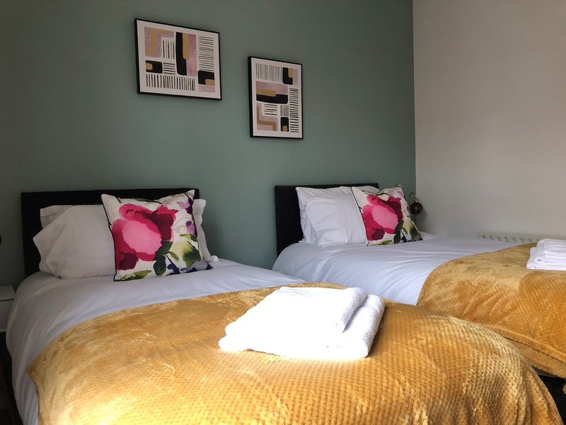 Bedroom with two single beds, sage green wall, framed artwork, pink patterned pillows