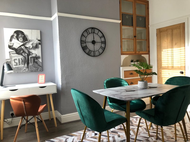 Modern dining room with marble table, green chairs, wall clock and framed artwork