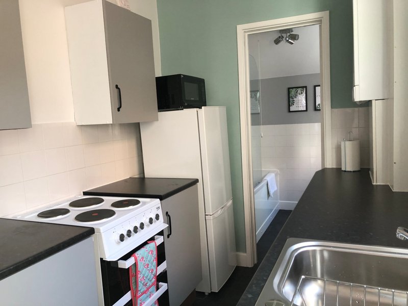 Kitchen with white cooker, black countertop, white cabinetry and open doorway to bedroom