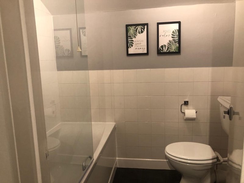 Clean bathroom with toilet, bathtub, shower enclosure and framed botanical wall art