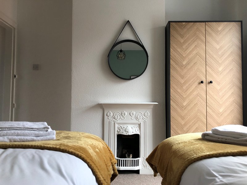 Twin bedroom with yellow bedding, decorative mirror, fireplace and herringbone wardrobe