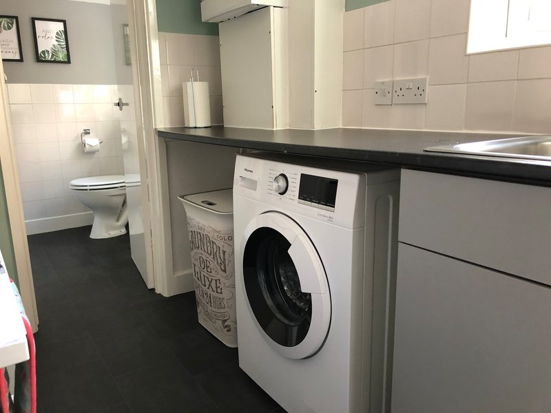 Modern kitchen with white washing machine, dark countertop, and toilet visible through doorway