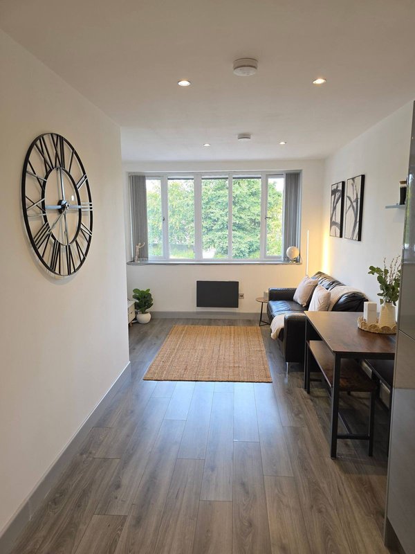 Modern studio interior with wooden flooring, wall clock, desk area, sofa and large window