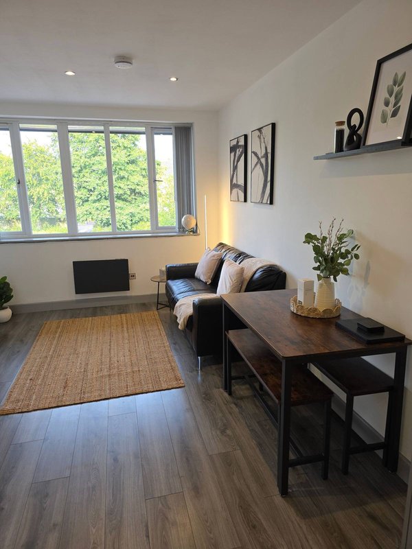 Modern living room with sofa, wooden console table, laptop, large windows and potted plant