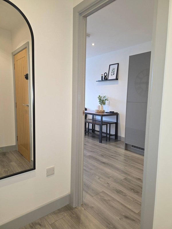 Hallway with arched mirror leading to modern living room with desk and potted plant