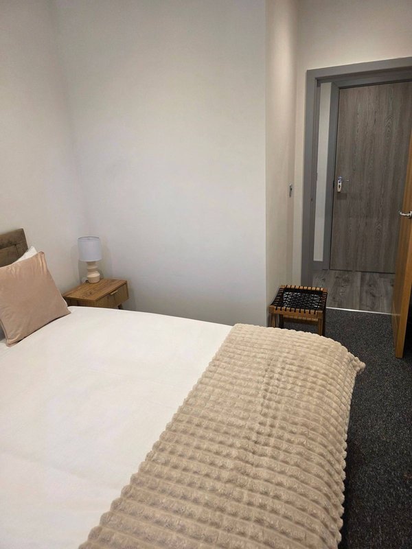 Bedroom with single bed, wooden bedside table, cream cushion, and grey door