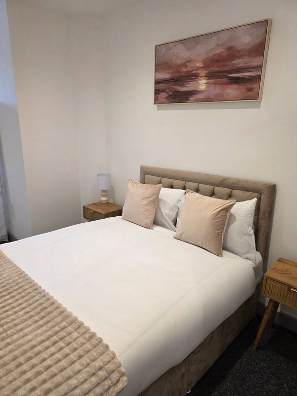 Bedroom with double bed, beige headboard, decorative pillows and framed landscape artwork on wall
