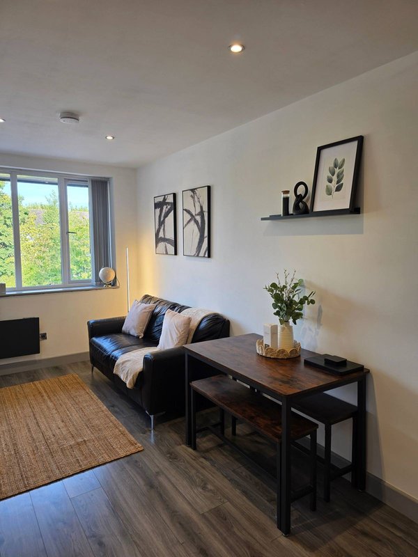 Modern living room with black sofa, wooden desk, framed wall art and large window