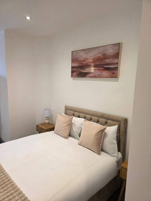 Bedroom with double bed, upholstered headboard, decorative pillows, and framed sunset artwork