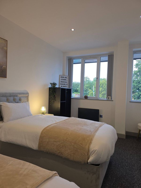 Bright bedroom with two single beds, bedside lamp, and large windows overlooking garden