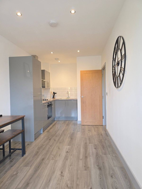 Modern kitchen and dining area with gray cabinetry, wooden floor, wall clock