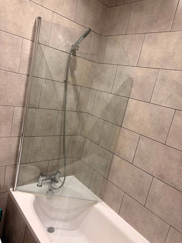 Bathroom with white bathtub, glass shower screen and beige tile walls