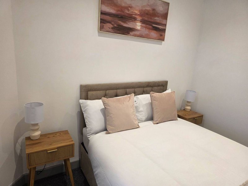 Bedroom with double bed, upholstered headboard, decorative pillows, wooden nightstand, and framed artwork above bed