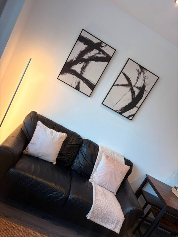 Modern living room with black leather sofa, white and pink cushions, wall art and warm lighting