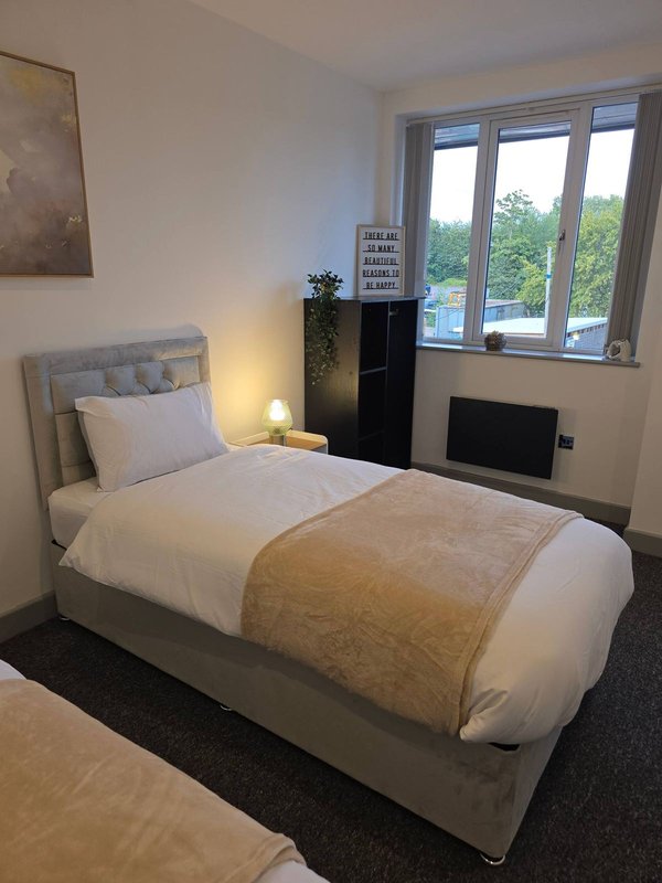 Single bedroom with upholstered bed, bedside lamp, framed wall art, and large windows overlooking garden