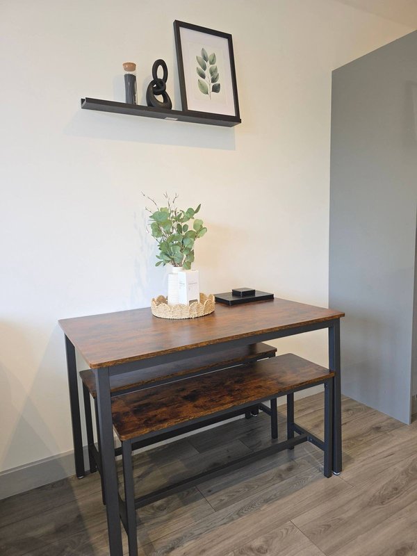 Wooden desk with bench seating, potted plant, and wall shelf with framed botanical print