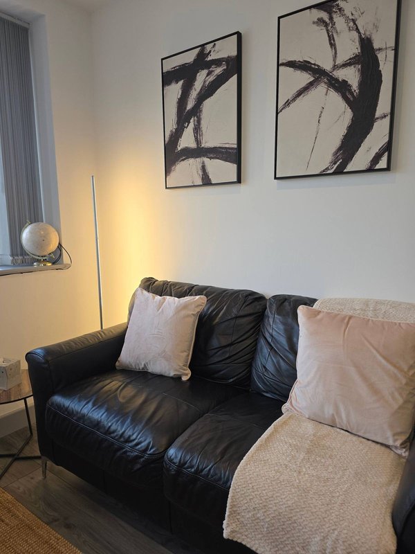 Living room with black leather sofa, decorative cushions, framed wall art, and floor lamp