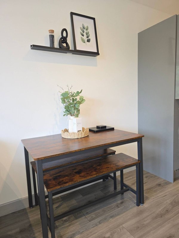 Dining table with bench seating, potted plant, and wall shelf with framed botanicals.