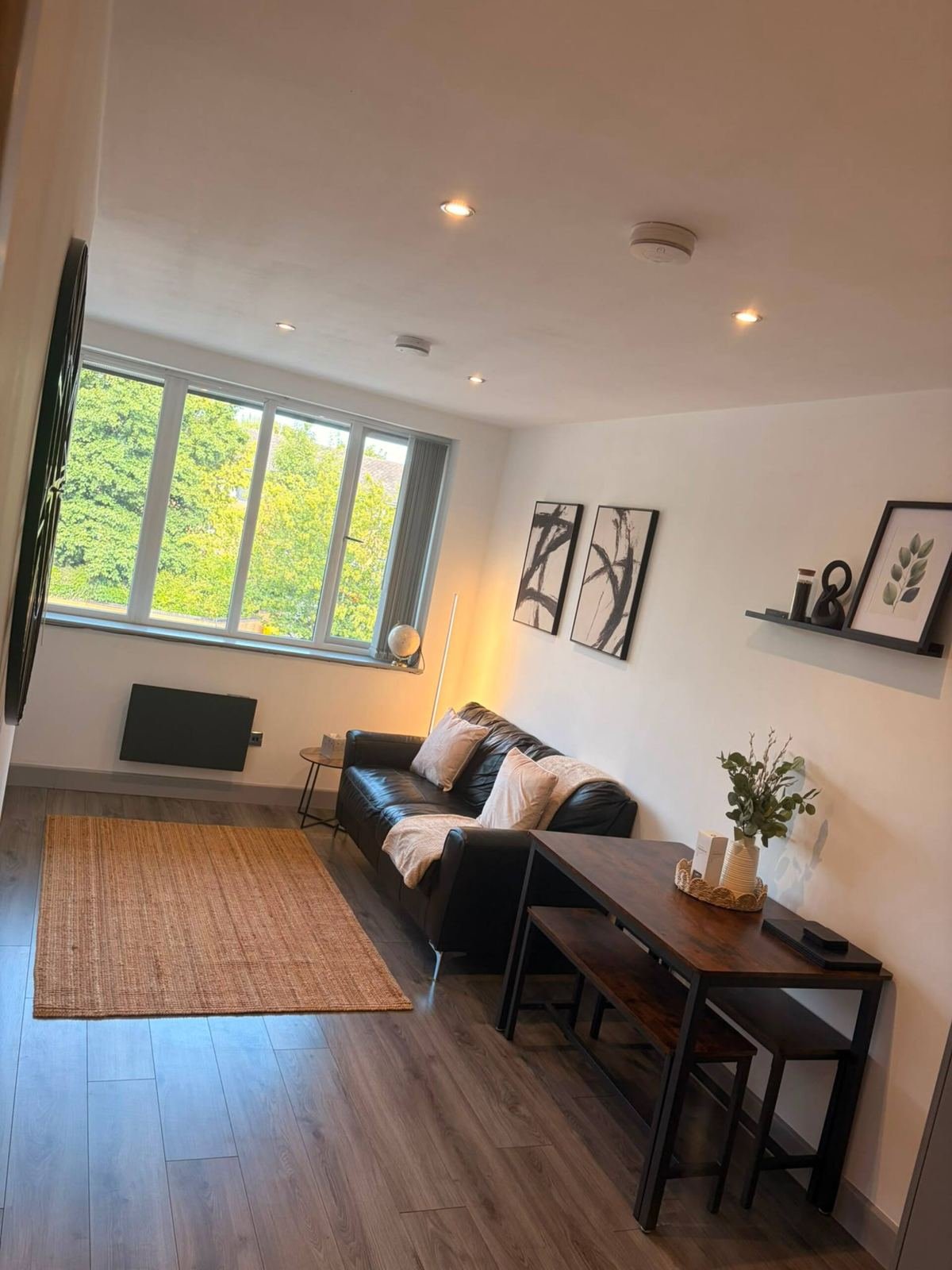 Modern living room with black sofa, wooden desk, large window overlooking garden