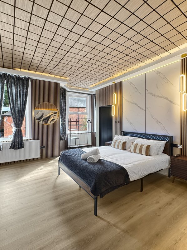 Modern bedroom with double bed, marble headboard, patterned curtains and geometric ceiling