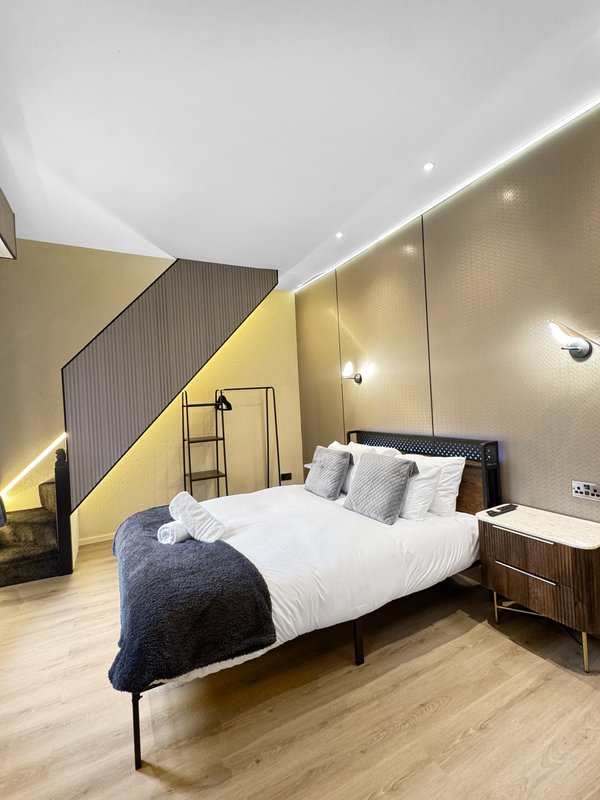 Modern bedroom with double bed, yellow accent wall, wooden flooring and recessed lighting