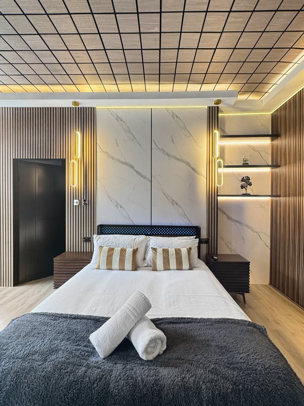 Modern bedroom with double bed, marble headboard, striped pillows and rolled towels