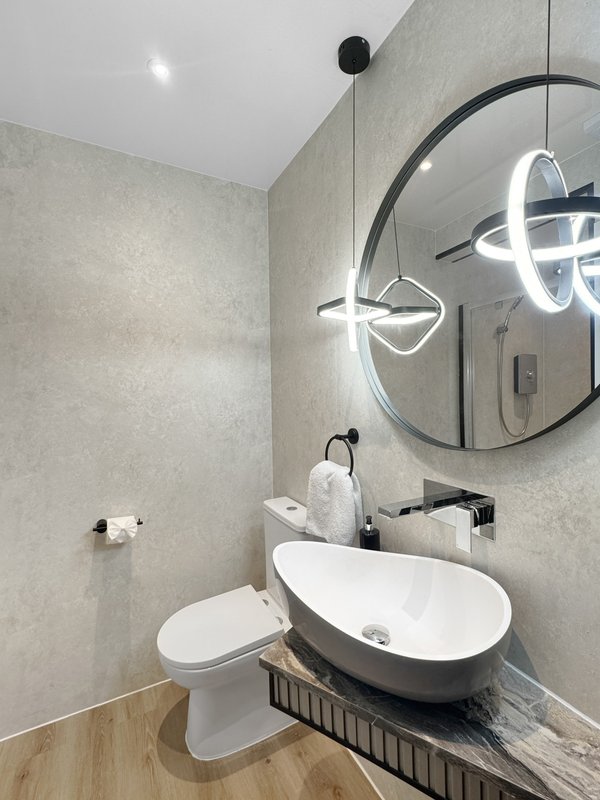 Modern bathroom with white vessel sink, toilet, round mirror and pendant lighting