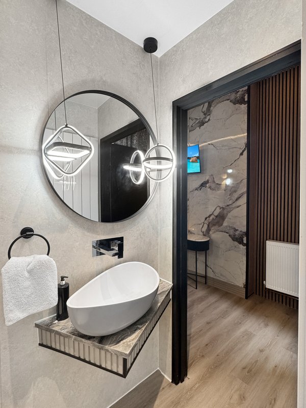 Modern bathroom with white oval sink, round mirror, pendant lights and wooden floor
