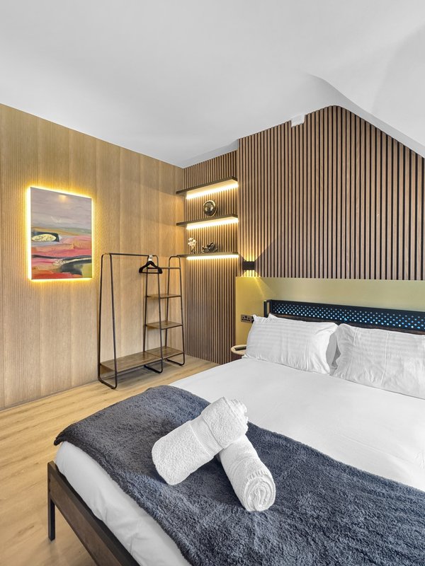 Modern bedroom with double bed, wooden flooring, illuminated wall art, and contemporary wood-paneled accent wall