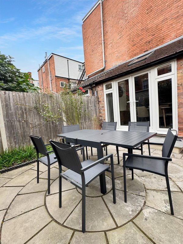 Outdoor patio with black dining table, four chairs, brick building and wooden fence