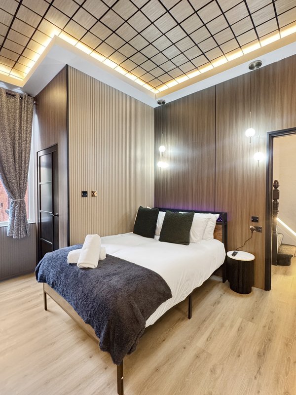 Modern bedroom with double bed, dark blue bedding, wooden wall paneling and geometric ceiling