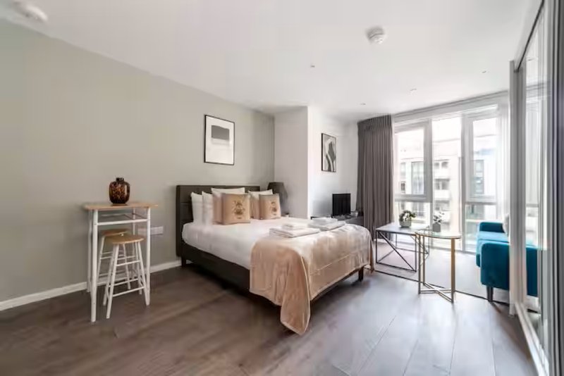 Modern bedroom with double bed, wooden floor, high windows and urban city views