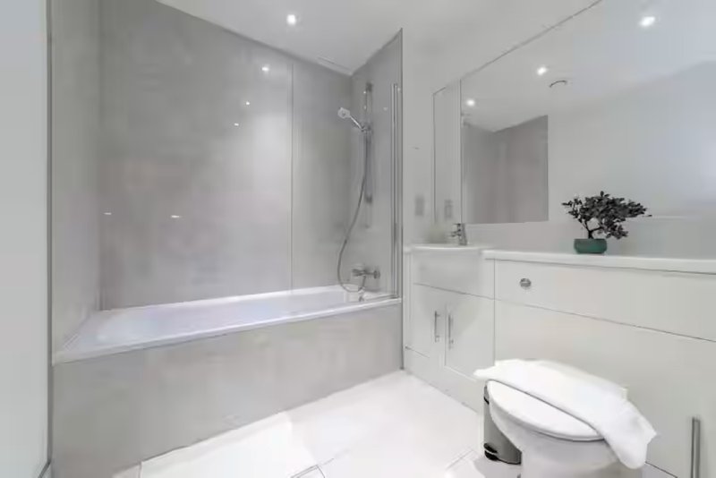 Modern bathroom with white toilet, vanity sink, mirror and bathtub with glass shower screen