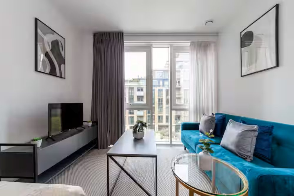 Modern living room with blue sofa, TV unit, glass coffee table and floor-to-ceiling windows