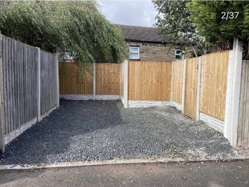 Driveway with gravel surface, wooden and grey fencing, stone house visible beyond