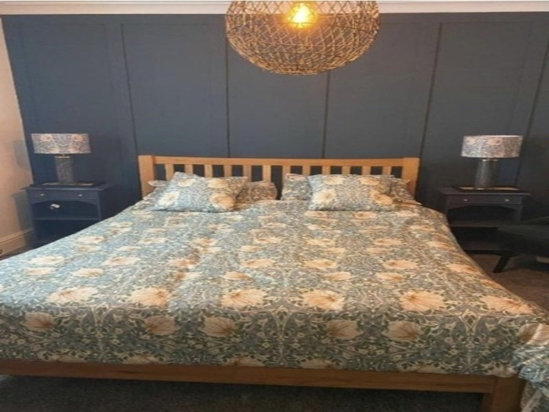 Modern bedroom with wooden bed frame, patterned duvet, dark blue walls and pendant lighting