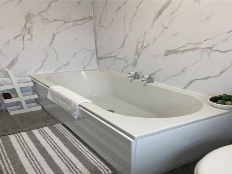Modern bathroom with freestanding white bathtub, marble-effect wall tiles and striped bath mat