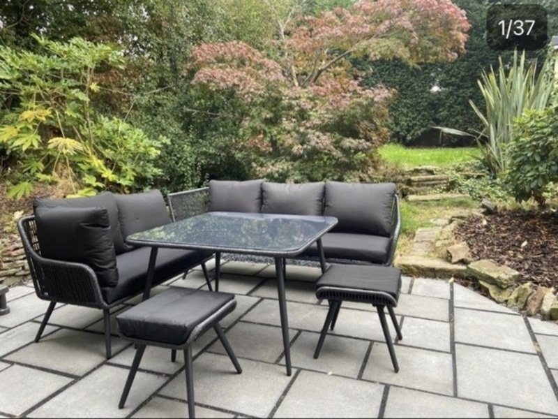 Garden patio with black outdoor furniture set and surrounding trees and shrubs