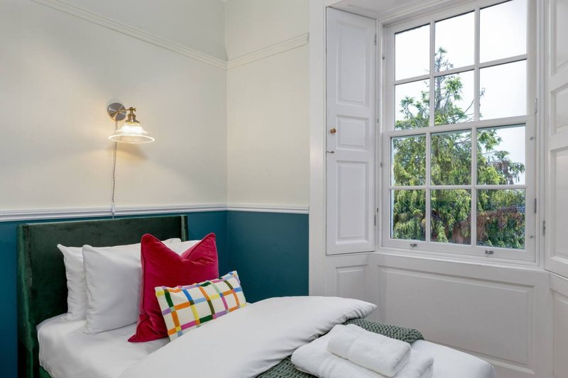 Bright bedroom with single bed, green headboard, colorful pillows and tall sash window