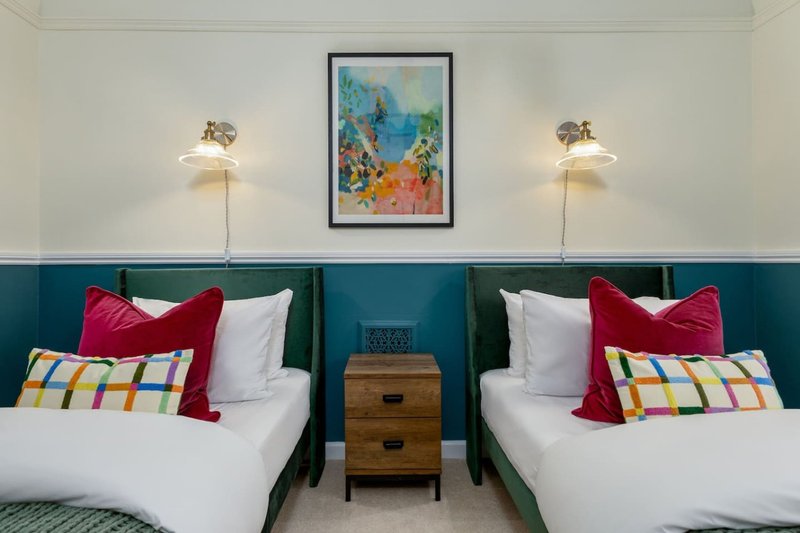 Twin bedroom with colorful pillows, bedside table, framed artwork, and wall sconces