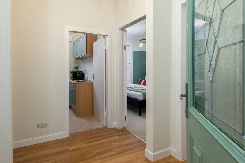 Open-plan hallway with wooden flooring, white walls, and doorways leading to kitchen and bedroom
