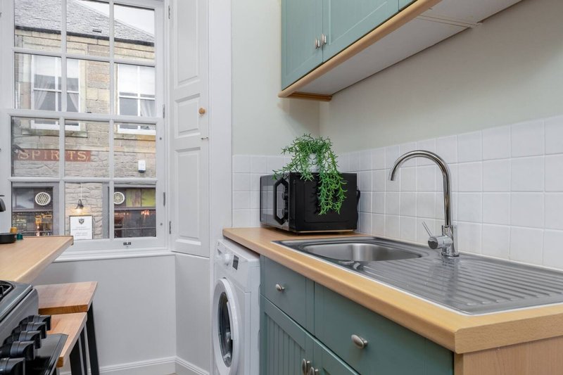 Modern kitchen with green cabinetry, wooden countertop, sink and washing machine