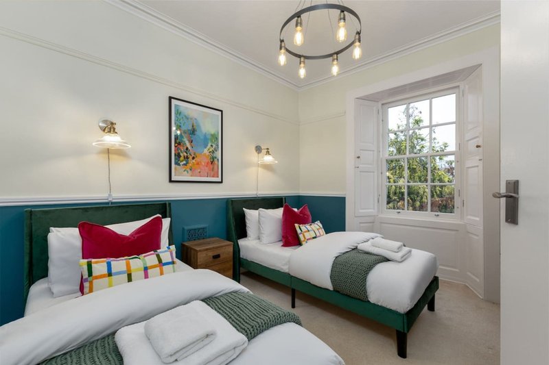Twin bedroom with green upholstered headboards, white bedding, red cushions, pendant ceiling light