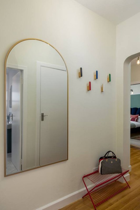 Hallway with arched mirror, wooden floor, red bench seat and small wall decorations