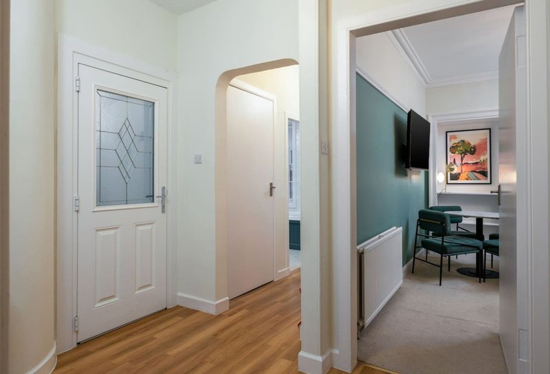 Modern hallway with wooden flooring, white walls, geometric patterned door, leading to bedroom with desk