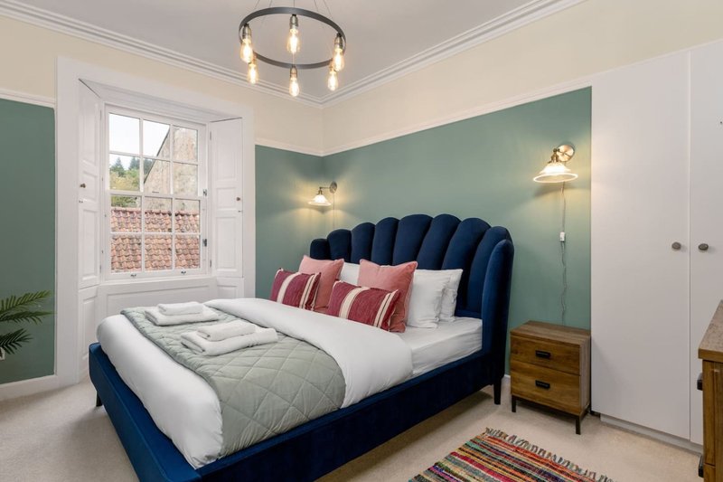 Bedroom with blue velvet bed, sage green accent wall, pendant lighting and wooden bedside table