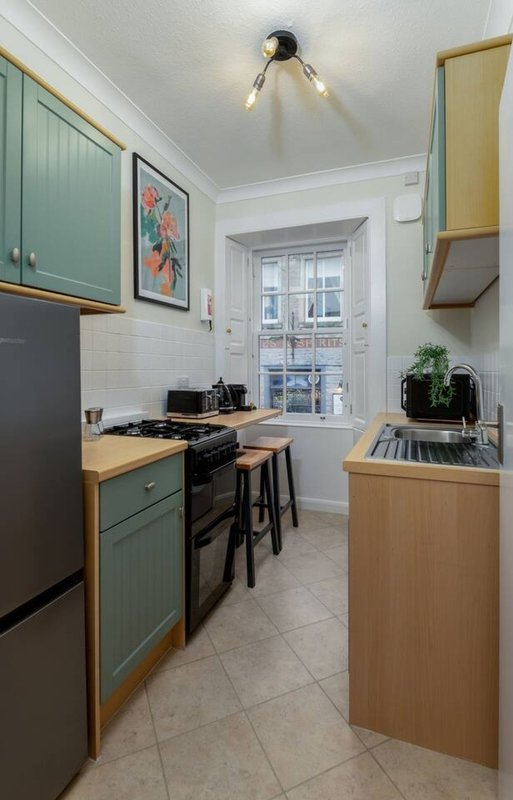 Modern kitchen with green cabinetry, wooden countertops, black appliances and white subway tiles