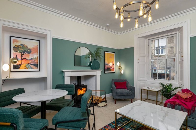 Modern living room with teal walls, fireplace, round dining table, armchairs and pendant lighting